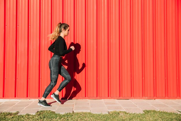 Giovane donna che corre vicino al muro rosso