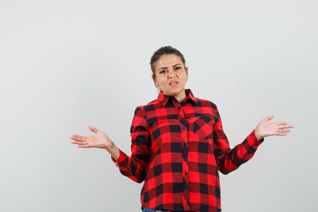 Giovane donna che diffonde le palme aperte in camicia a quadri e sembra ragionevole. vista frontale.