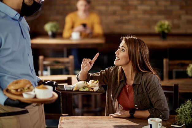 Giovane donna che discute con il cameriere che sta servendo il suo cibo in un pub