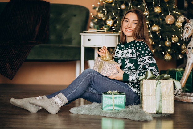 Giovane donna che disimballa regalo di Natale dall'albero di Natale