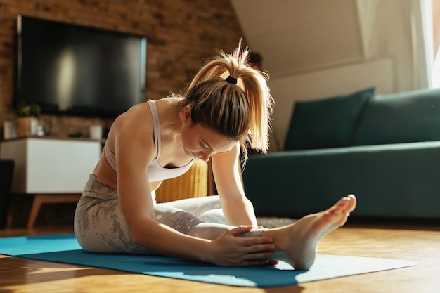 Giovane donna che fa esercizi di stretching sul pavimento a casa