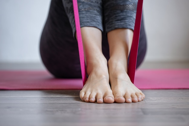 Giovane donna che fa esercizi sportivi con elastico a casa sul tappetino, fitness a casa, stretching e yoga.