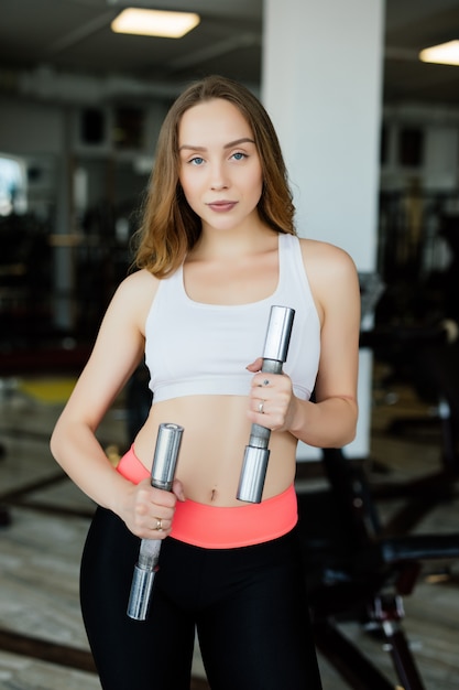 Giovane donna che fa esercizio con manubri in palestra fitness club.