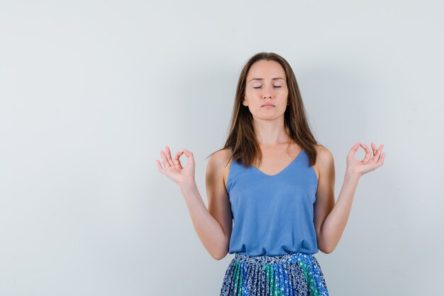 Giovane donna che fa meditazione con gli occhi chiusi in canottiera, gonna e sembra rilassata