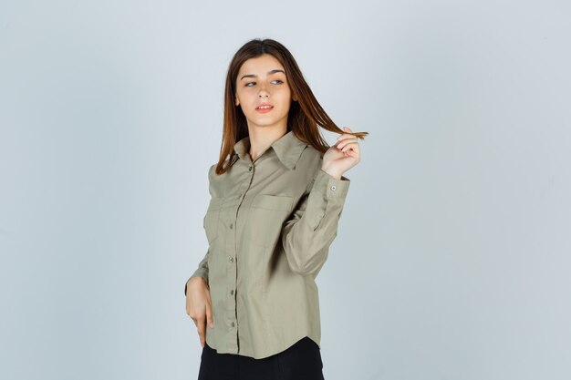 Giovane donna che fa roteare i capelli tra le dita mentre distoglie lo sguardo in camicia, gonna e sembra pensierosa. vista frontale.