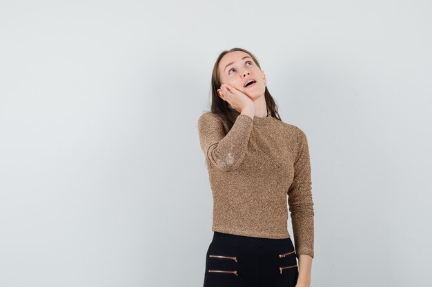 Giovane donna che finge di parlare al telefono in maglione dorato e pantaloni neri e sembra pensierosa. vista frontale.