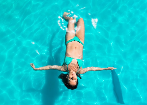 Giovane donna che galleggia sul retro in piscina