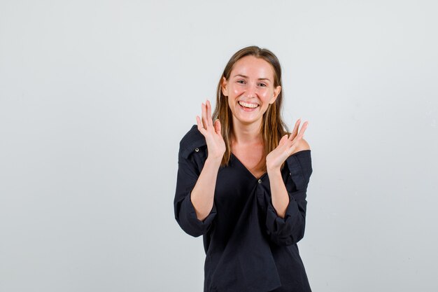 Giovane donna che gesturing con le mani e sorridente in camicia, pantaloncini e guardando allegra. vista frontale.