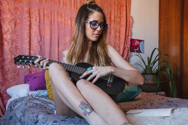 Giovane donna che gioca ukulele sul letto
