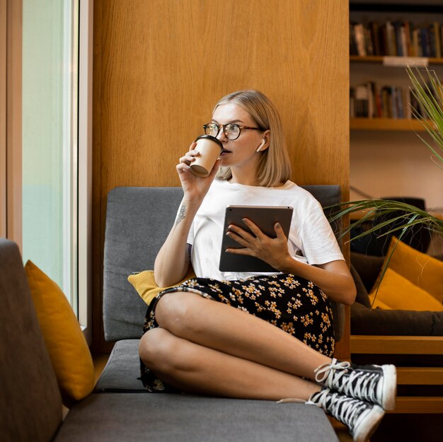 Giovane donna che gode del caffè in biblioteca
