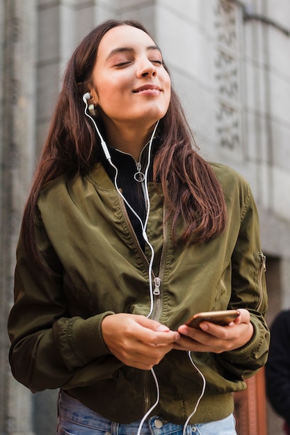 Giovane donna che gode della musica sul trasduttore auricolare per mezzo del telefono mobile