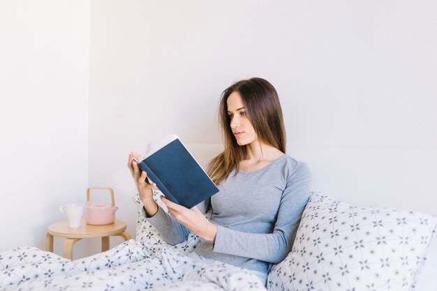 Giovane donna che gode leggendo a letto