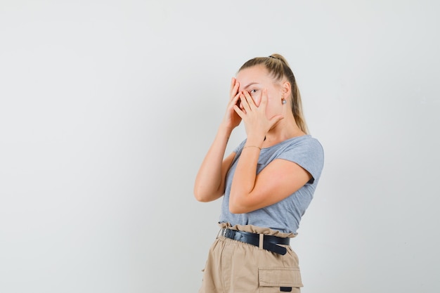 Giovane donna che guarda attraverso le dita in maglietta e pantaloni e sembra elegante