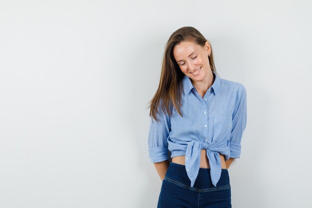 Giovane donna che guarda con le mani sulla schiena in camicia blu, pantaloni e sembra ottimista