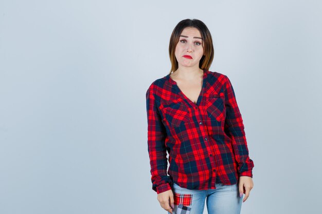 Giovane donna che guarda davanti in camicia a quadri e sembra sarcastica. vista frontale.