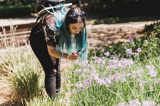 Giovane donna che guarda i fiori selvaggi tramite la lente d&#39;ingrandimento