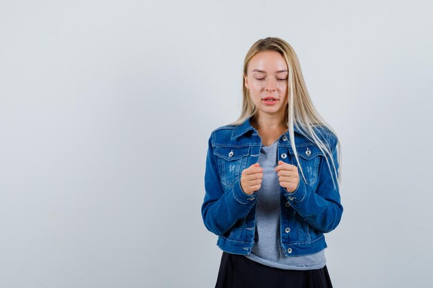 Giovane donna che guarda i pugni in maglietta, giacca di jeans, gonna e sembra pensierosa