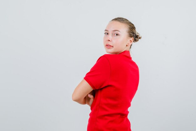 Giovane donna che guarda indietro con le braccia incrociate in maglietta rossa e guardando fiducioso. .