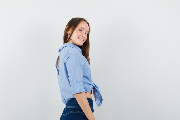 Giovane donna che guarda l'obbiettivo in camicia blu, pantaloni e sembra gioviale