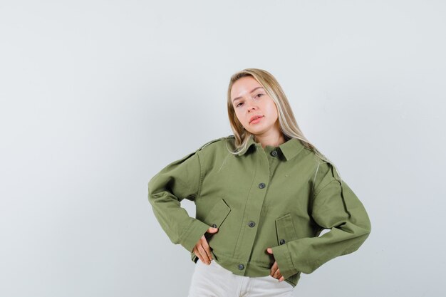 Giovane donna che guarda l'obbiettivo in giacca verde, jeans e guardando soddisfatto. vista frontale.