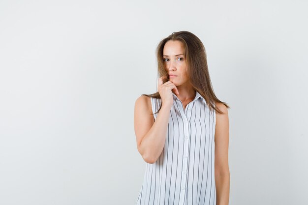 Giovane donna che guarda l'obbiettivo in t-shirt e guardando pensieroso, vista frontale.