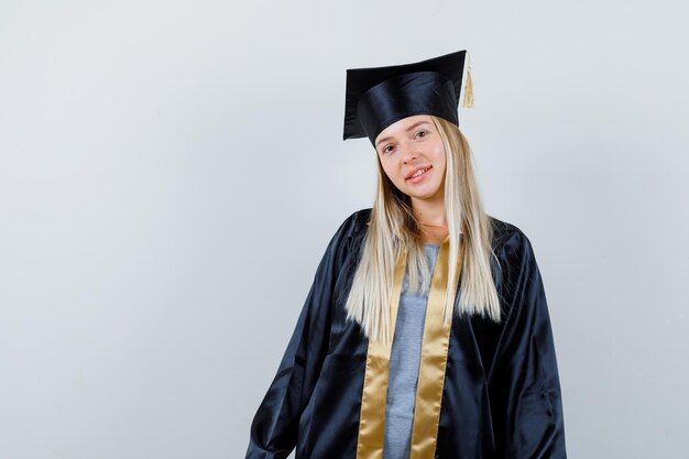 Giovane donna che guarda l'obbiettivo in uniforme laureata e sembra allegra.