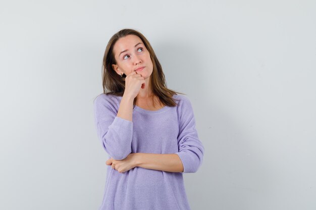 Giovane donna che guarda lontano in camicetta lilla e guardando pensieroso