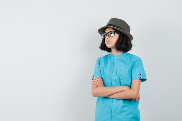 Giovane donna che guarda lontano in camicia blu, occhiali e guardando pensieroso