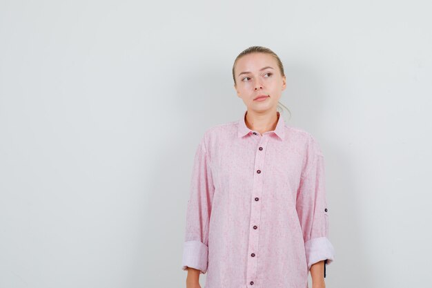 Giovane donna che guarda lontano in camicia rosa e guardando pensieroso