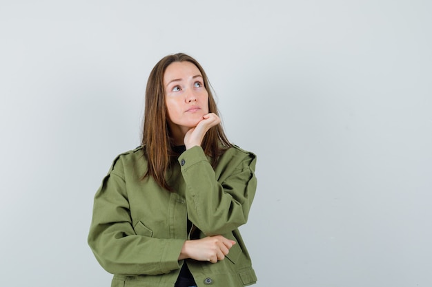 Giovane donna che guarda lontano mentre si appoggia la mano in giacca verde e guardando pensieroso. vista frontale.