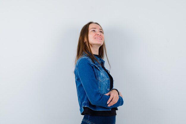 Giovane donna che guarda verso l'alto in camicetta, giacca e sembra sognante, vista frontale.