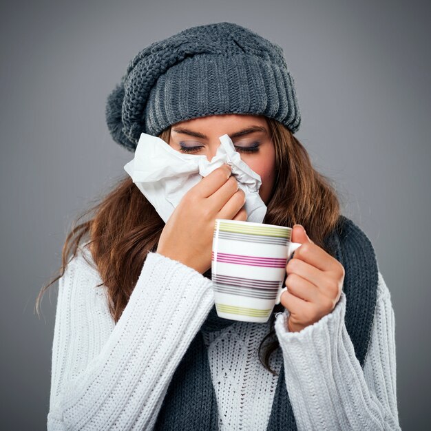 Giovane donna che ha influenza e che soffia il naso al fazzoletto