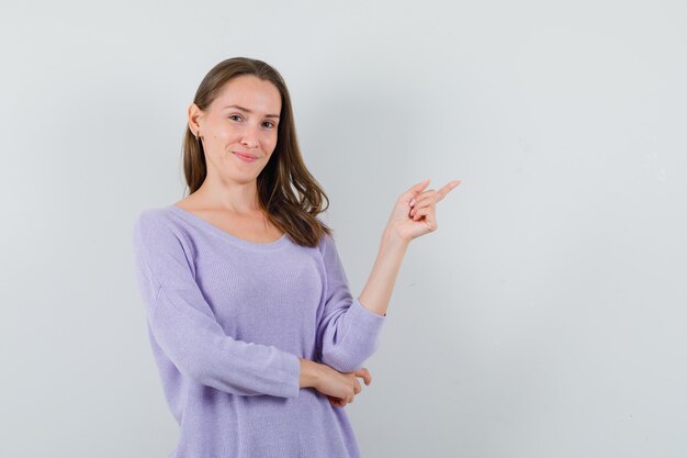 Giovane donna che indica da parte in camicia casual e sembra allegra. vista frontale.