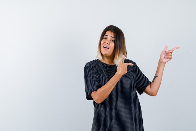 Giovane donna che indica il lato destro in abito polo e sembra esitante, vista frontale.