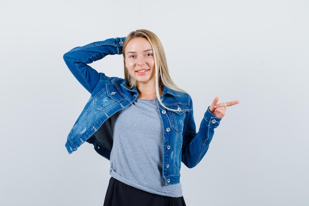 Giovane donna che indica il lato destro in t-shirt, giacca di jeans, gonna e sembra seducente.