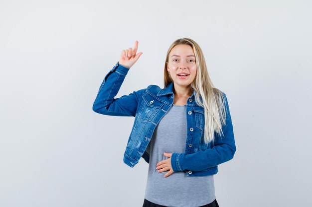 Giovane donna che indica in t-shirt, giacca di jeans, gonna e sembra felice