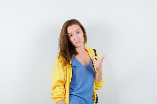 Giovane donna che indica se stessa in t-shirt, giacca e sembra perplessa, vista frontale.