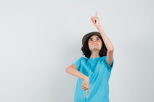 Giovane donna che indica su e giù in camicia blu, cappello e sguardo concentrato.