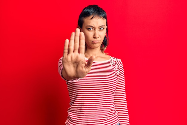 Giovane donna che indossa abiti casual che smette di cantare con il palmo dell'espressione di avvertimento della mano con gesto negativo e serio sul viso