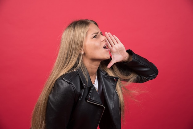 Giovane donna che indossa abiti casual gridando e urlando forte a lato con la mano sulla bocca