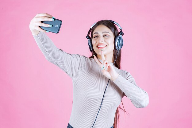 Giovane donna che indossa le cuffie e prendendo il suo selfie