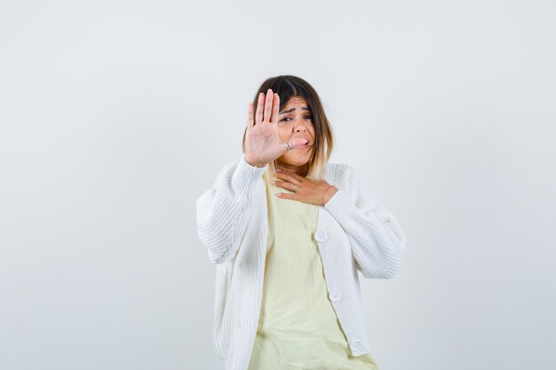 Giovane donna che indossa un cardigan bianco che mostra il gesto di arresto