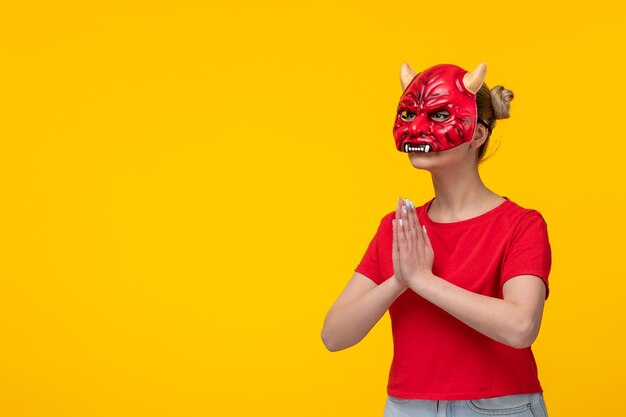Giovane donna che indossa una maschera da diavolo spaventoso che implora sfondo giallo halloween brutto