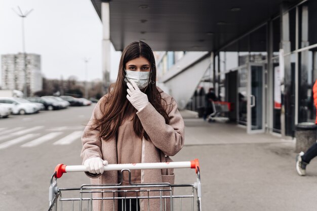 Giovane donna che indossa una maschera protettiva contro il coronavirus 2019-nCoV che spinge un carrello. Concetto di coronavirus