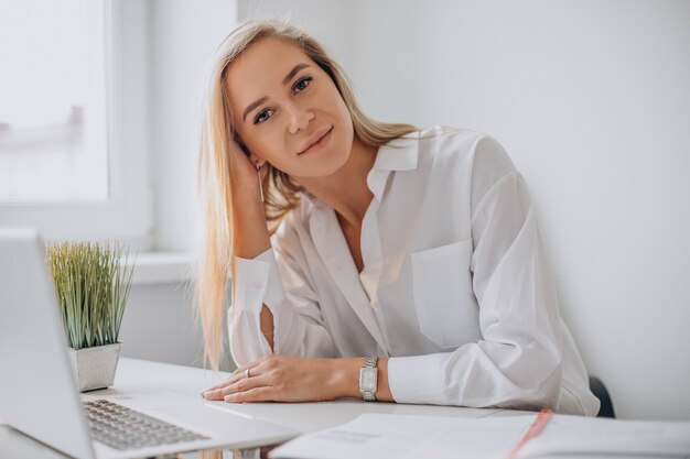 Giovane donna che lavora al computer portatile in ufficio ed esamina la macchina fotografica