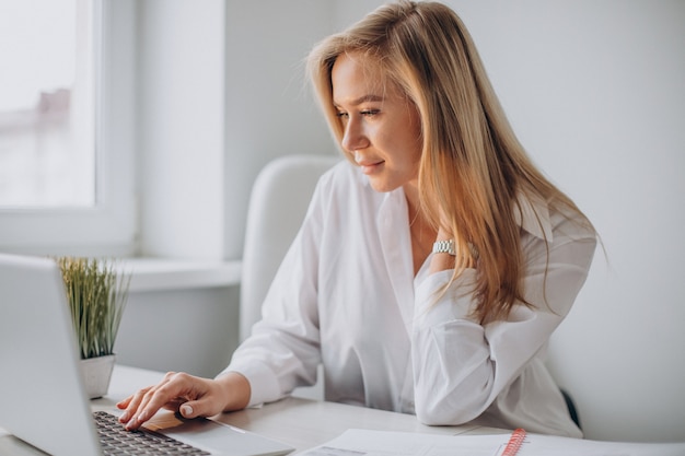 Giovane donna che lavora al computer portatile in ufficio ed esamina la macchina fotografica