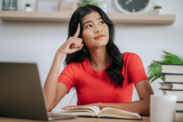 Giovane donna che lavora con il computer portatile sulla scrivania e pensa a risolvere i problemi