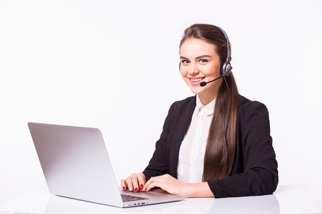 Giovane donna che lavora in ufficio con laptop e cuffie sul muro bianco, servizio clienti e call center.