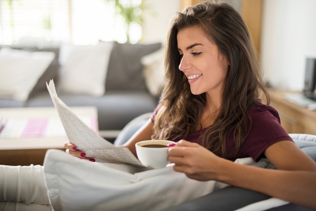 Giovane donna che legge il giornale e che beve caffè