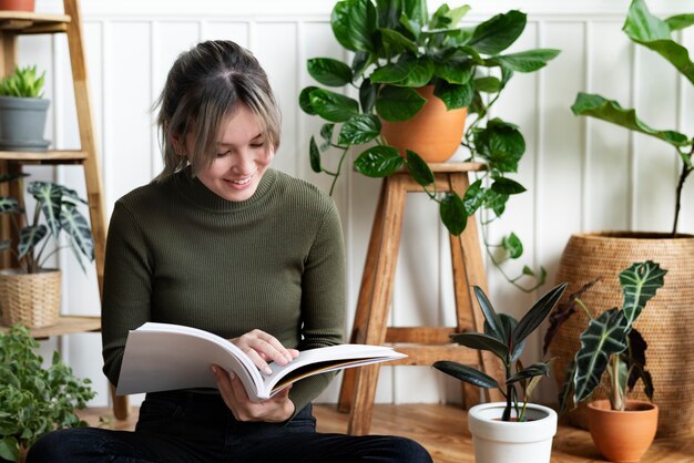 Giovane donna che legge un libro sul giardinaggio circondata da piante in vaso